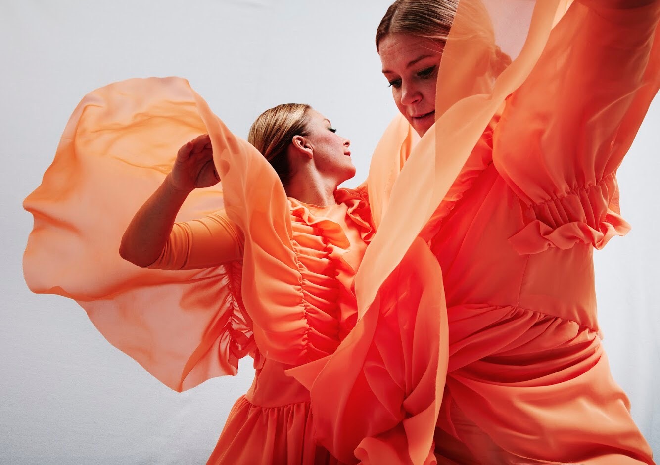 Två dansare viftar med armarna och har orange kostym på.