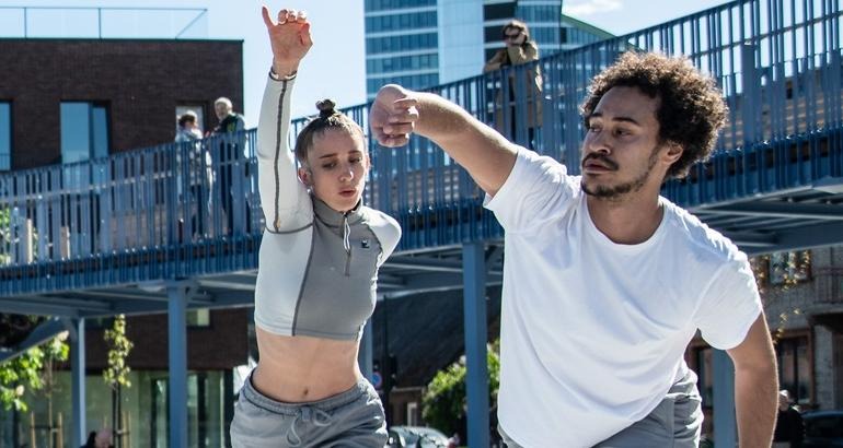 Två dansare som lyfter höger arm upp och sidan.